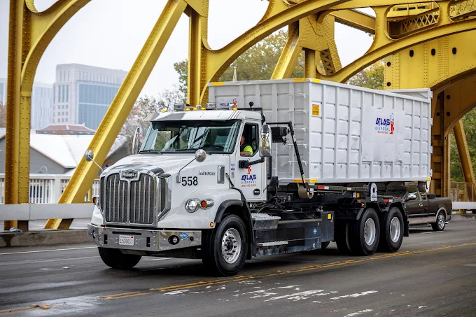 An Atlas Disposal truck delivering a roll off dumpster delivery to a customer who has prepared their driveway for the delivery. 